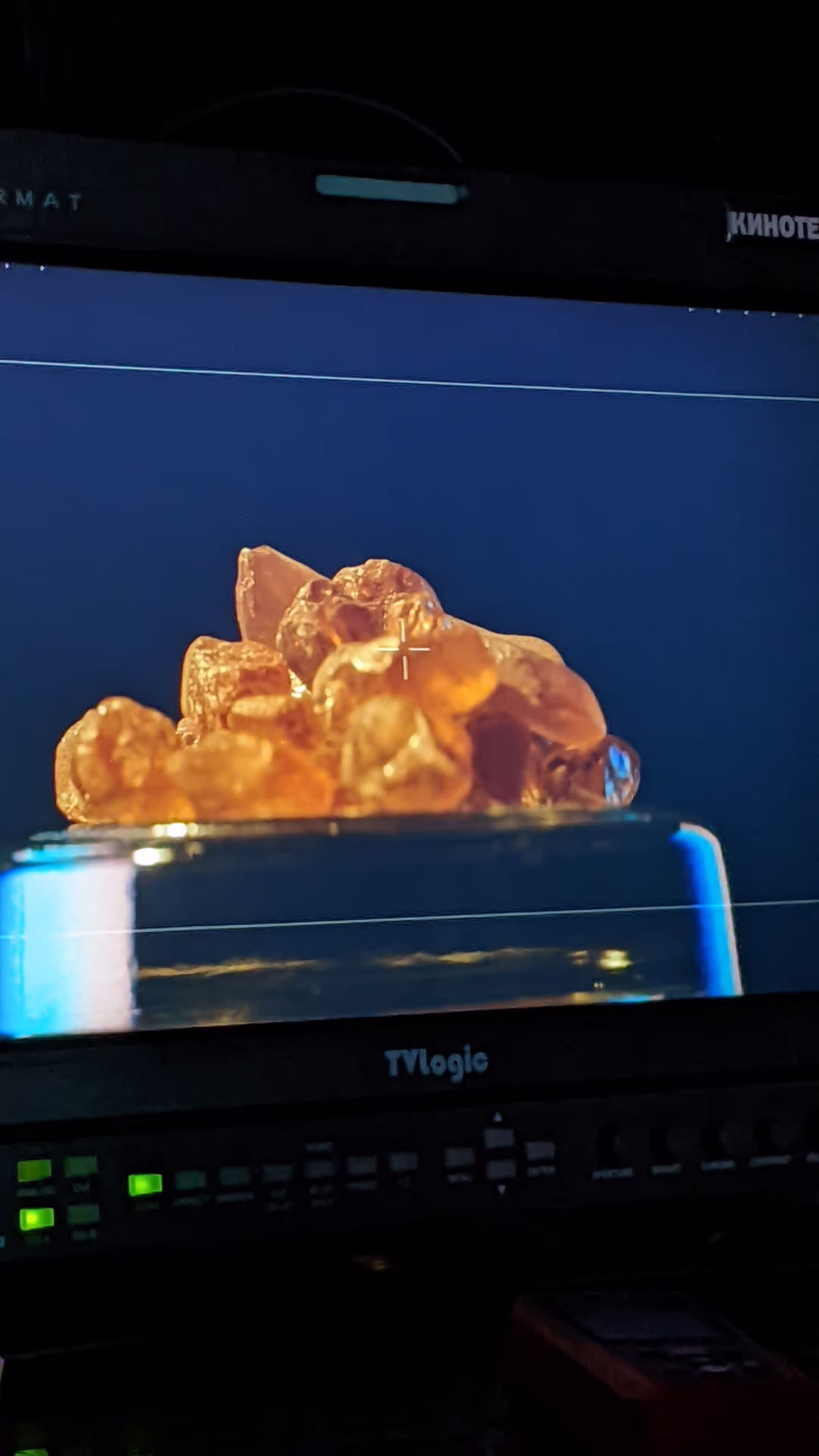 Video monitor shows orange translucent crystals on pedestal with camera controls below.