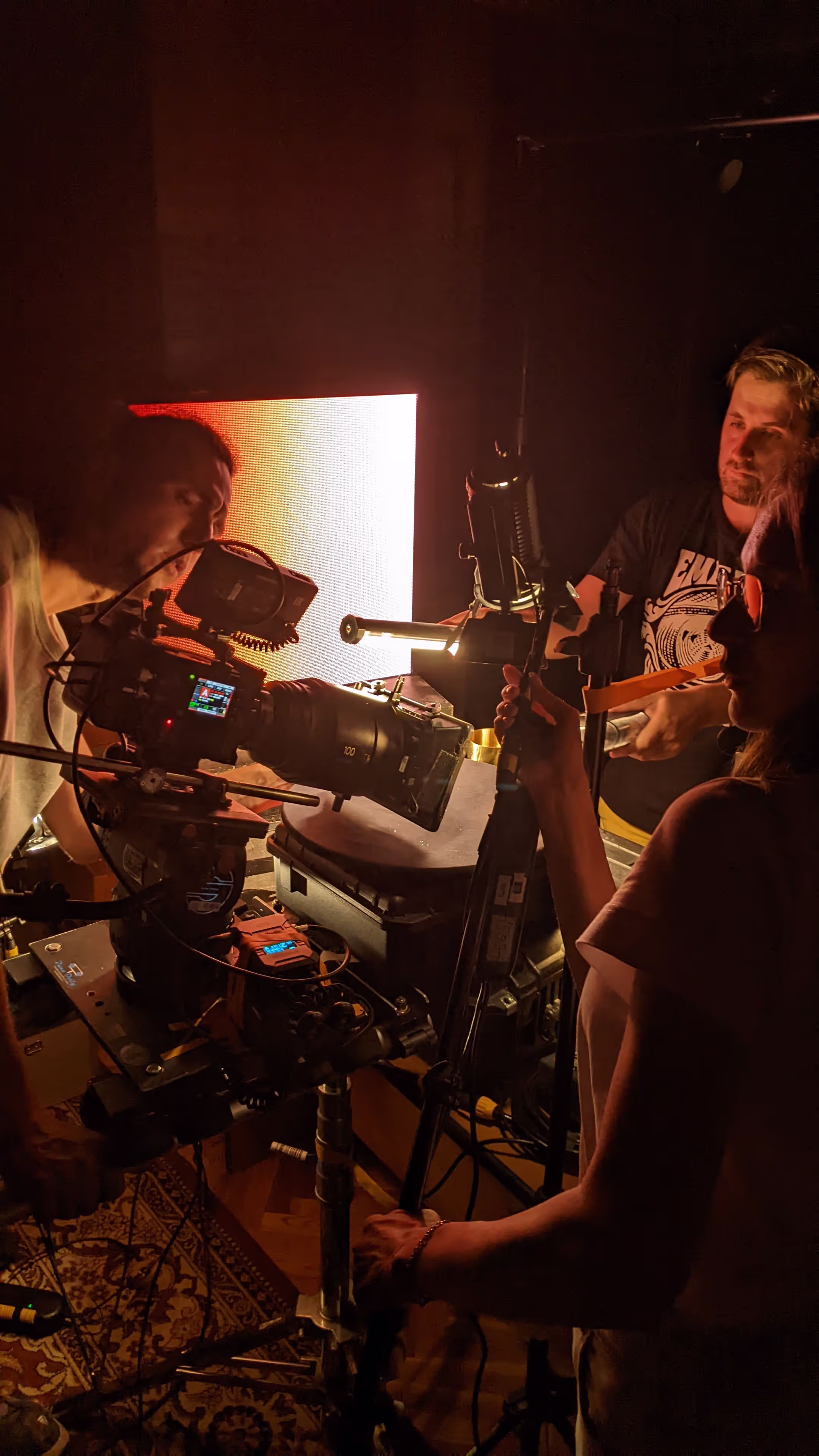 Three people adjust camera, lights and reflector around white box with green mineral on turntable.