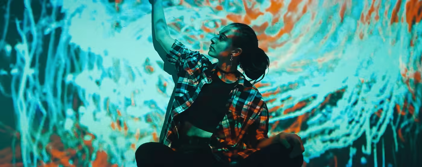 Person in plaid shirt surrounded by cyan and orange projections.