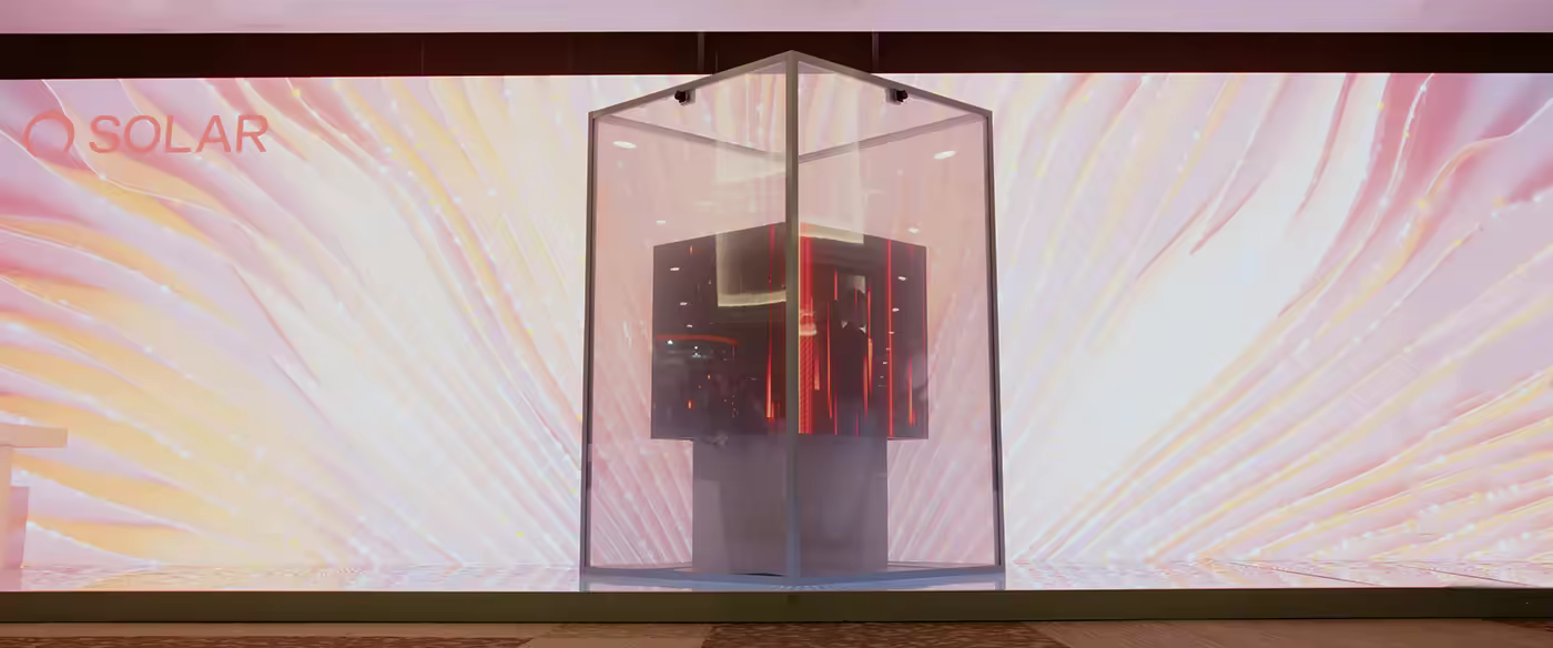 Glass case containing dark cube with red vertical lights on stage with pink-yellow waves.
